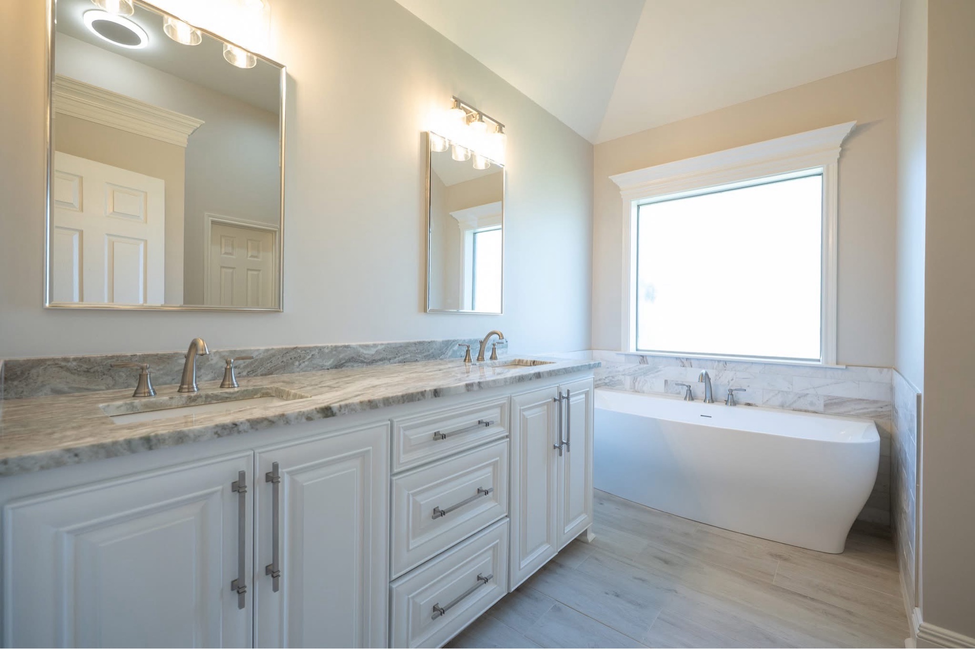 Master bath after — white shaker vanity, freestanding tub, marble wainscot